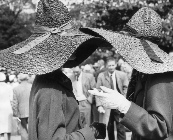 Two women wearing large, floppy brimmed, straw hats have a chat during a visit to the Chelsea Flower Show in 1963.
