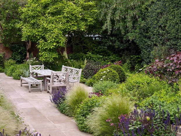 The spacious dining terrace is in the sunniest part of the garden, shielded from overlooking windows by a stand of trees that includes a large magnolia. Ornamental grasses and the deep-amethyst flower spikes of Salvia x sylvestris ‘Mainacht’ soften surrounding beds anchored with plump balls of yew.