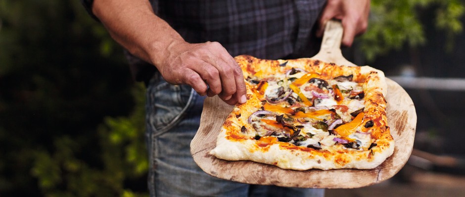 A pizza that has been cooked over a campfire has been placed on a wooded utensil and is ready to serve
